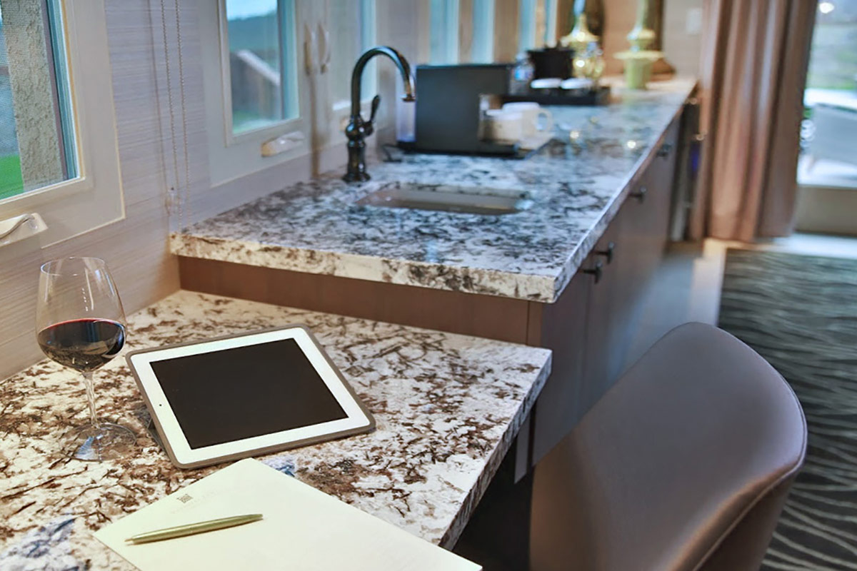 A glass of red wine, an iPad, a wirting pad with a pencil on top placed on a work space in the living room of the Vineyard Terrace Deluxe Suite at Vintners Resort. At the background is the wet bar.