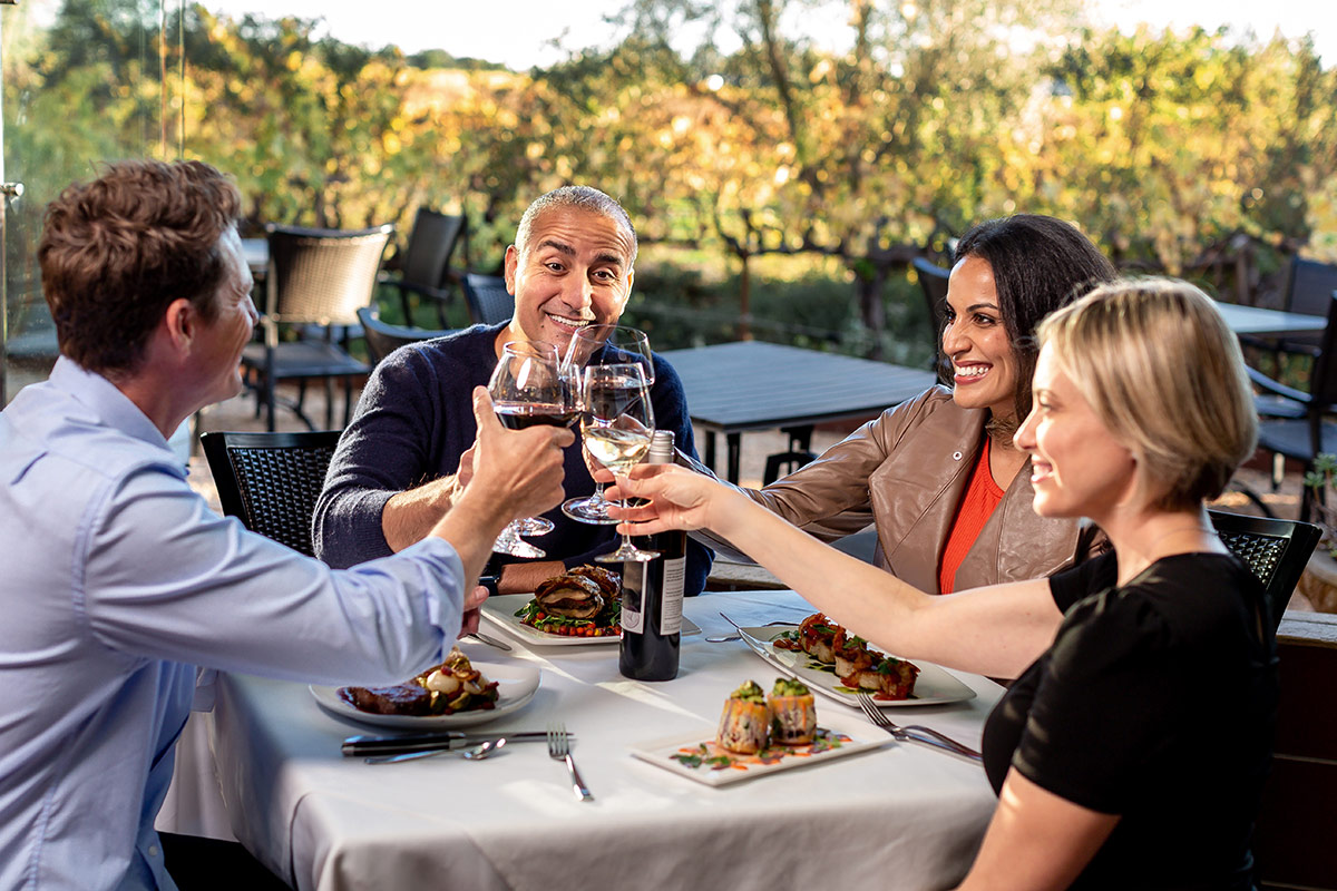 Four smiling guests dining at Vintners Resort and raising their wine glasses.