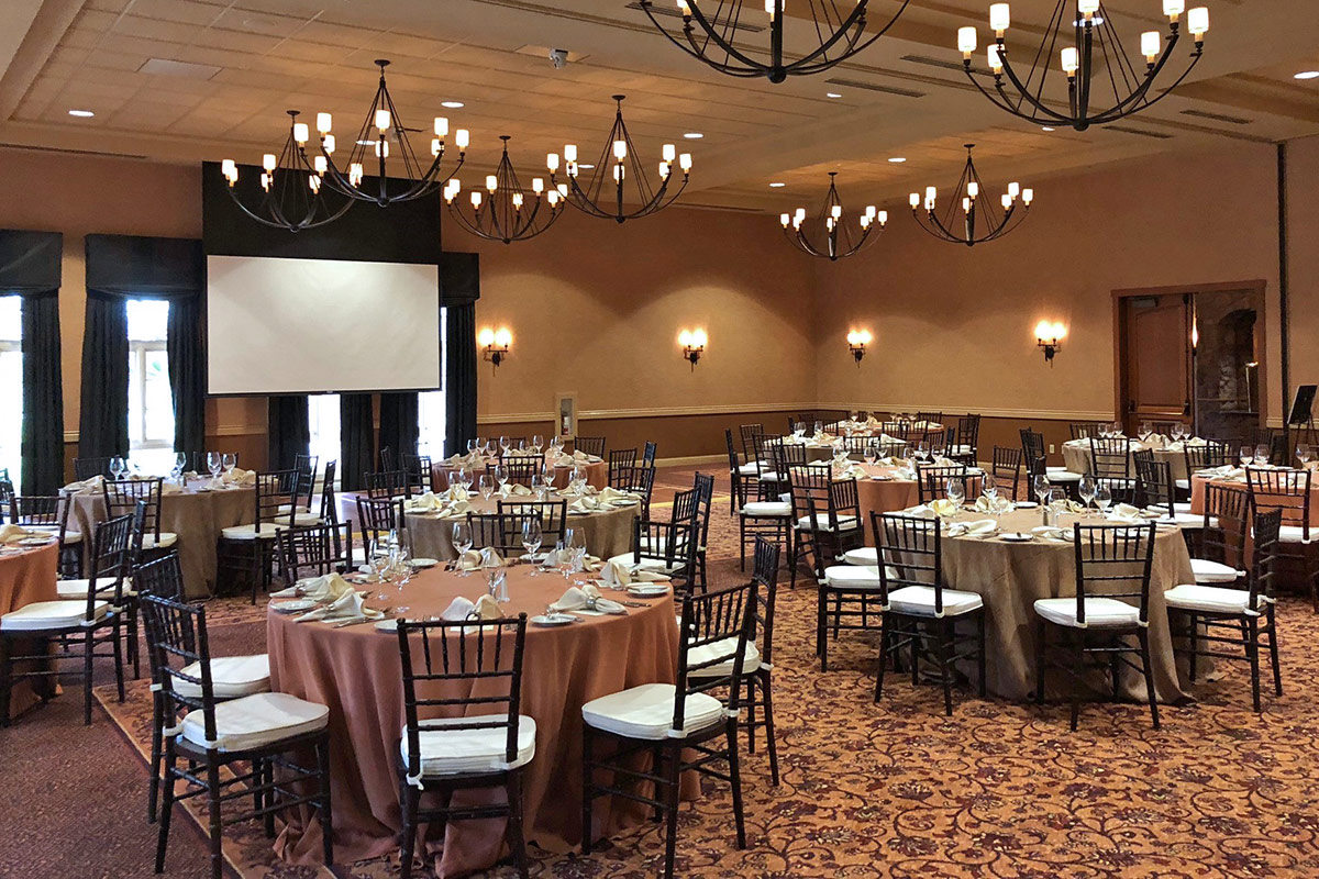 Banquet setting with table rounds for a private event in the Rose Ballroom at Vintners Resort. A projector screen at the back of the room.