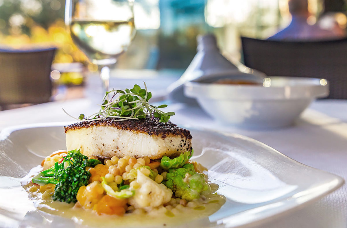 Served at John Ash & Co., a mouthwatering fish dish on a bed of locally sourced vegetables, complemented by a glass of white wine.
