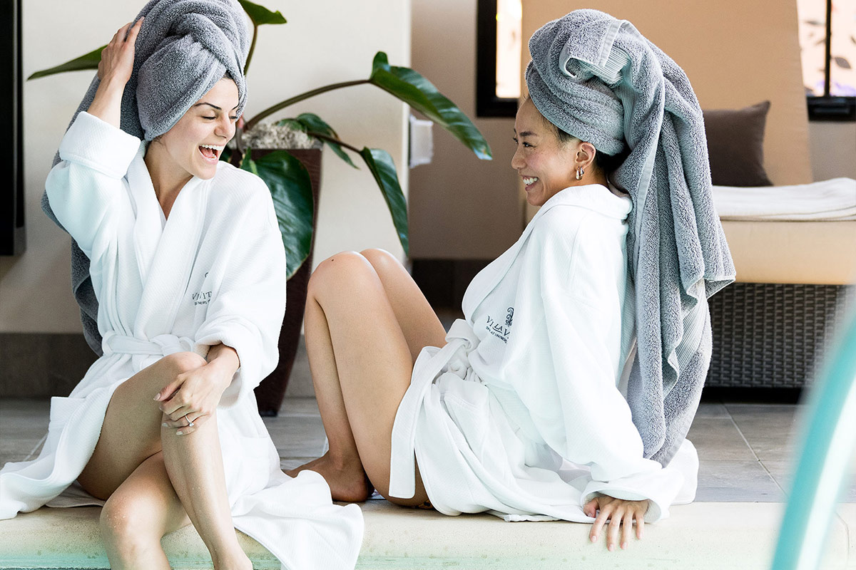 Two women wrapped their hair in towels, and enjoying a conversation by the indoor heated soaking pool at Vi La Vita Spa.