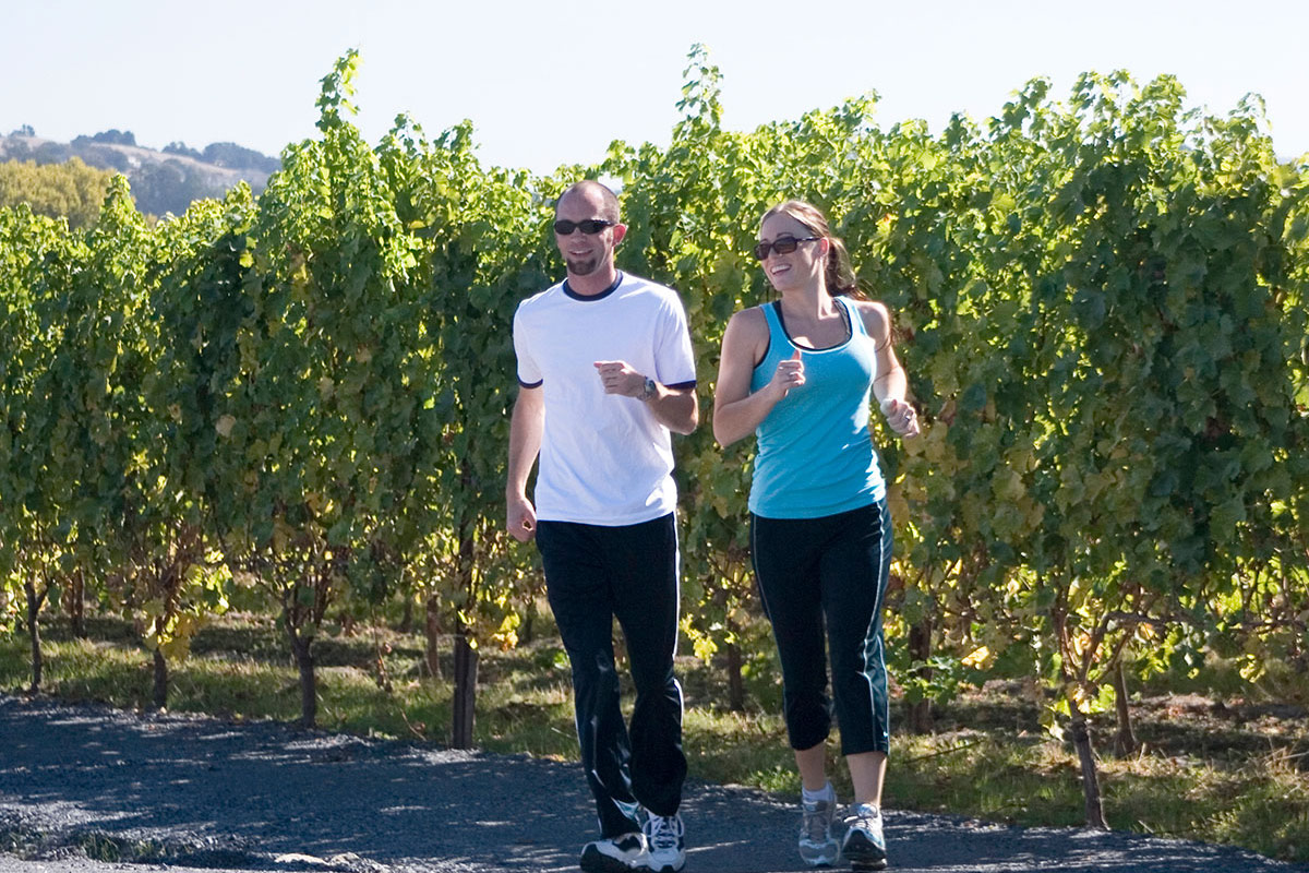 A man and a woman jogging through the 92 acres of lush vineyards at Vintners Resort.