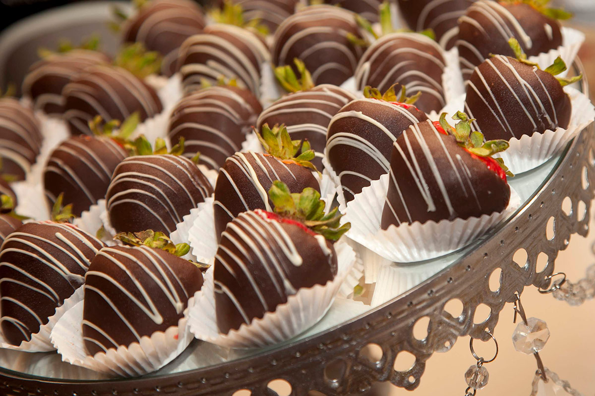 Chocolate covered strawberries with white chocolate drizzle served outside on a platter in white paper cupcake cups for celebratory purposes, at Vintners Resort's event center.