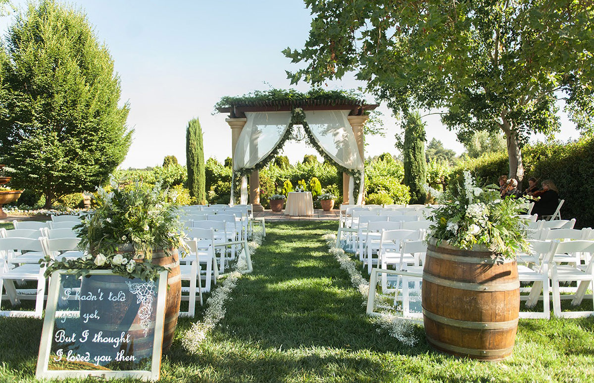 An outdoor wedding ceremony set up at Vintners Resort, with signage and flowers at the entrance, chairs on both sides of the aisle, and a beautifully decorated pavilion at the end.
