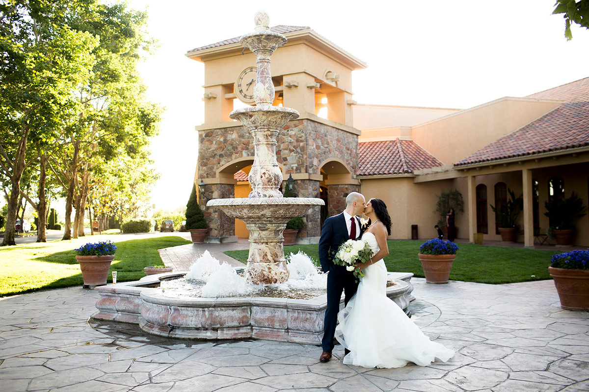 A wedding couple posing infront of the fountain and the 30 ft. European style stone clock Bell Tower at Vintners Resort.